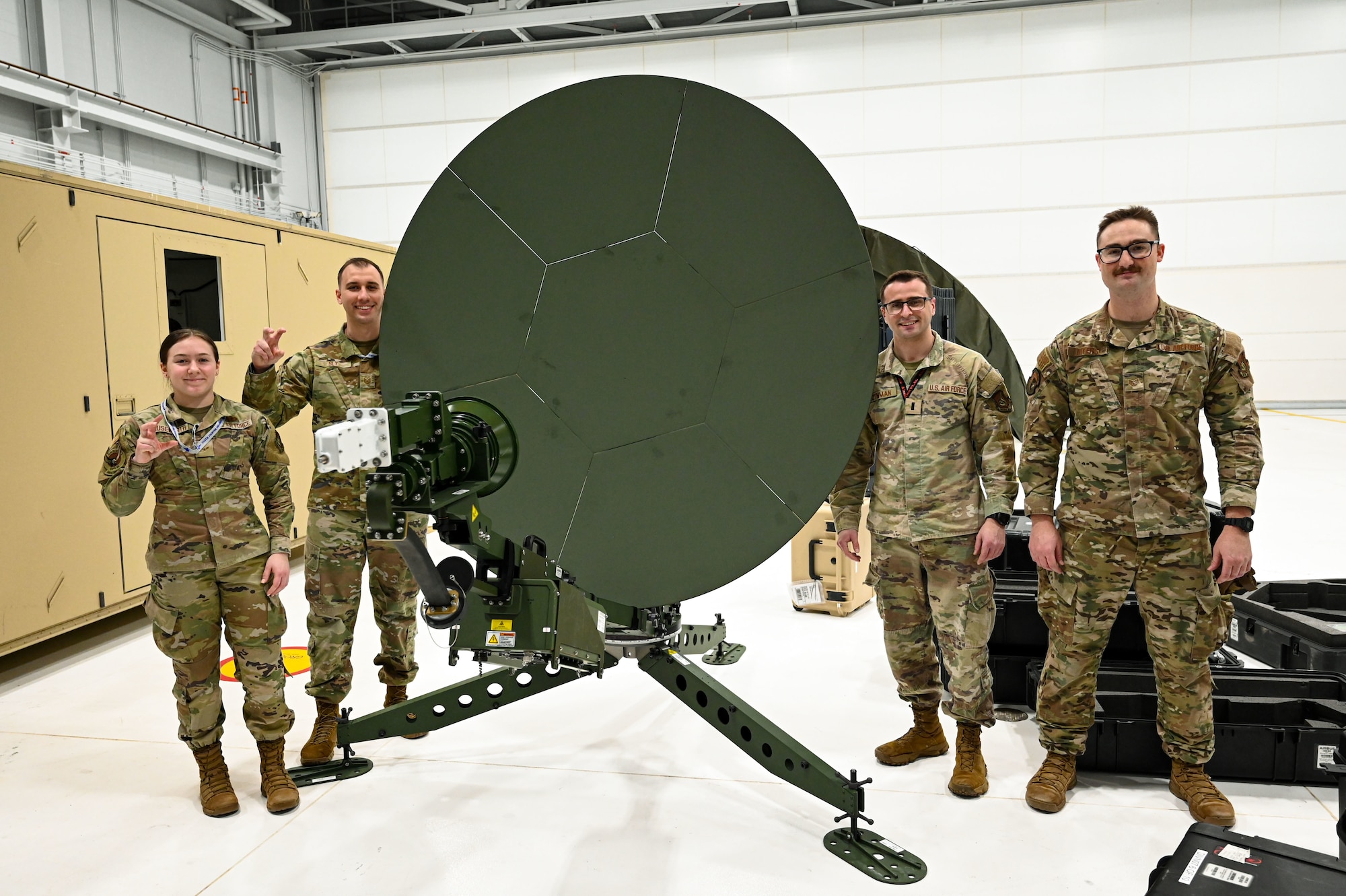 Airmen pose for a photo in front of a communication satellite