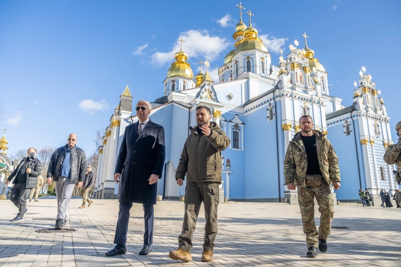 President Joe Biden walks with his Ukrainian counterpart in front of an ornate light blue building.