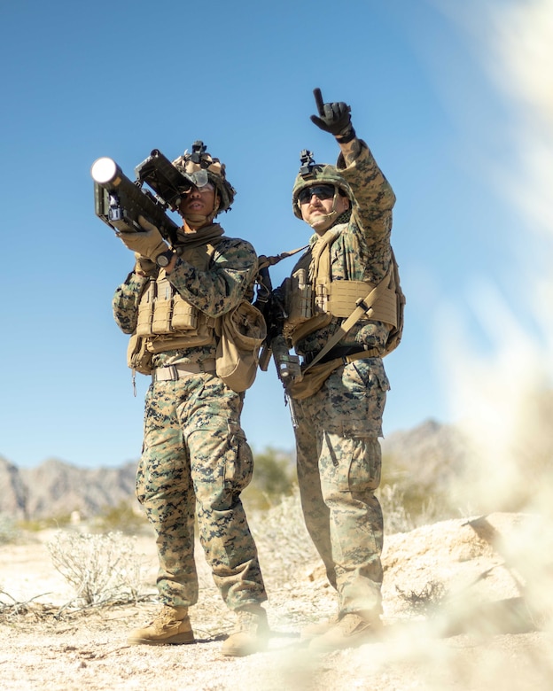 A Marine looks through the scope of a weapon as another Marine points .