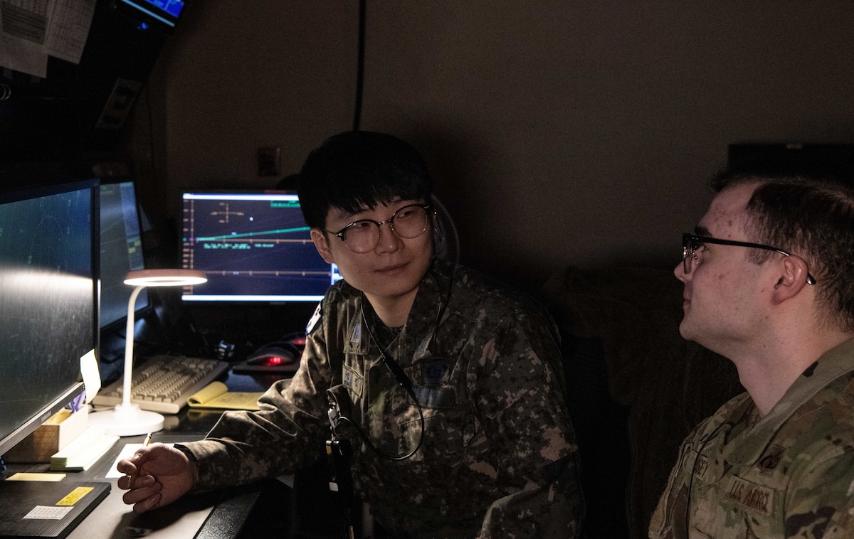 Republic of Korea Air Force Master Sgt. Seong Jin Kim (left), 38th Fighter Group operating branch radar controller, speaks with U.S. Air Force Staff Sgt. James Massey II, 8th Operations Support Squadron air traffic control (ATC) radar approach controller watch supervisor, at Kunsan Air Base, Republic of Korea, Feb. 16, 2023. When necessary, ROKAF personnel provided translation between different ATC facilities to remove any language barriers when needed. (U.S. Air Force photo by Staff Sgt. Sadie Colbert)