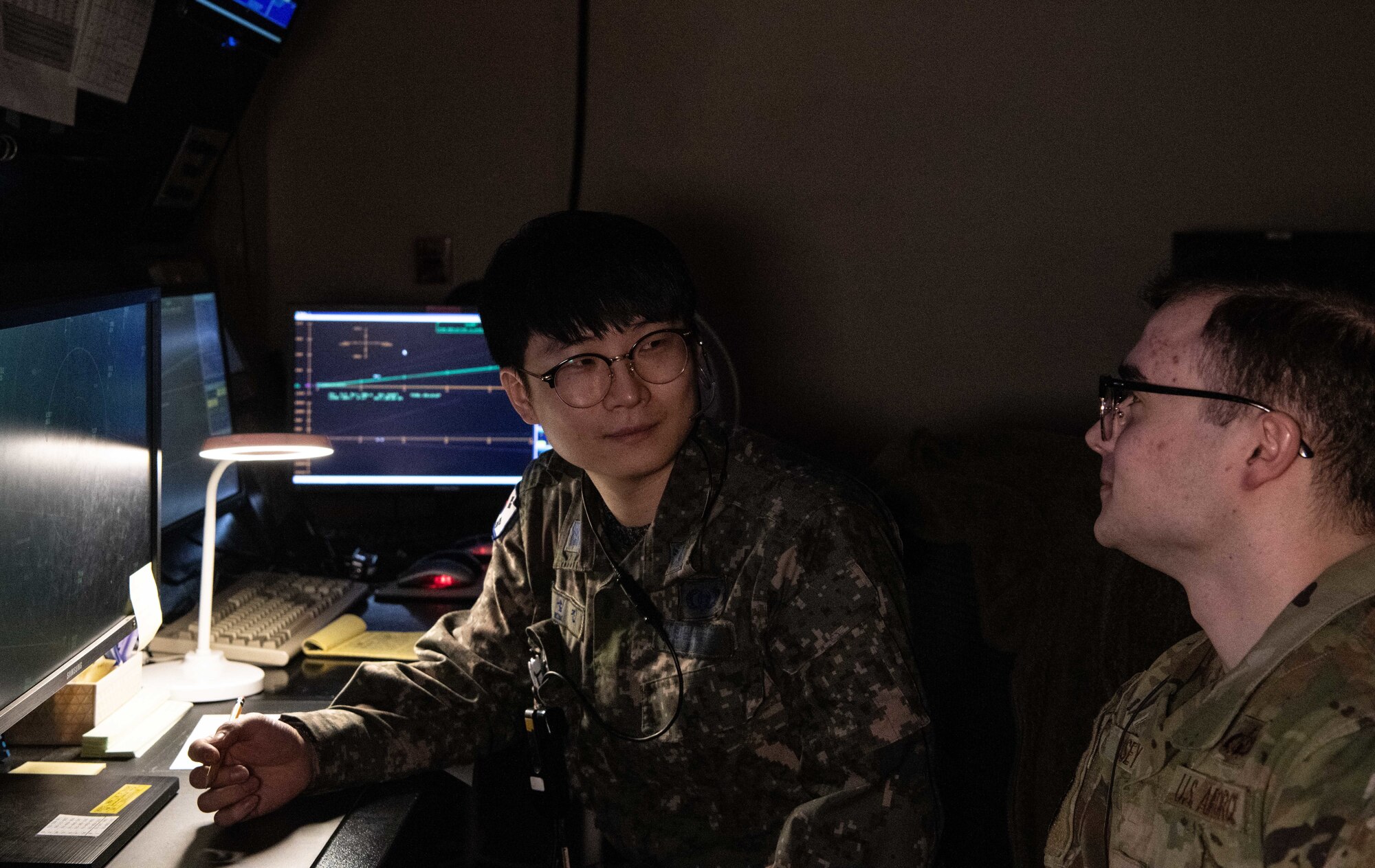 Republic of Korea Air Force Master Sgt. Seong Jin Kim (left), 38th Fighter Group operating branch radar controller, speaks with U.S. Air Force Staff Sgt. James Massey II, 8th Operations Support Squadron air traffic control (ATC) radar approach controller watch supervisor, at Kunsan Air Base, Republic of Korea, Feb. 16, 2023. When necessary, ROKAF personnel provided translation between different ATC facilities to remove any language barriers when needed. (U.S. Air Force photo by Staff Sgt. Sadie Colbert)
