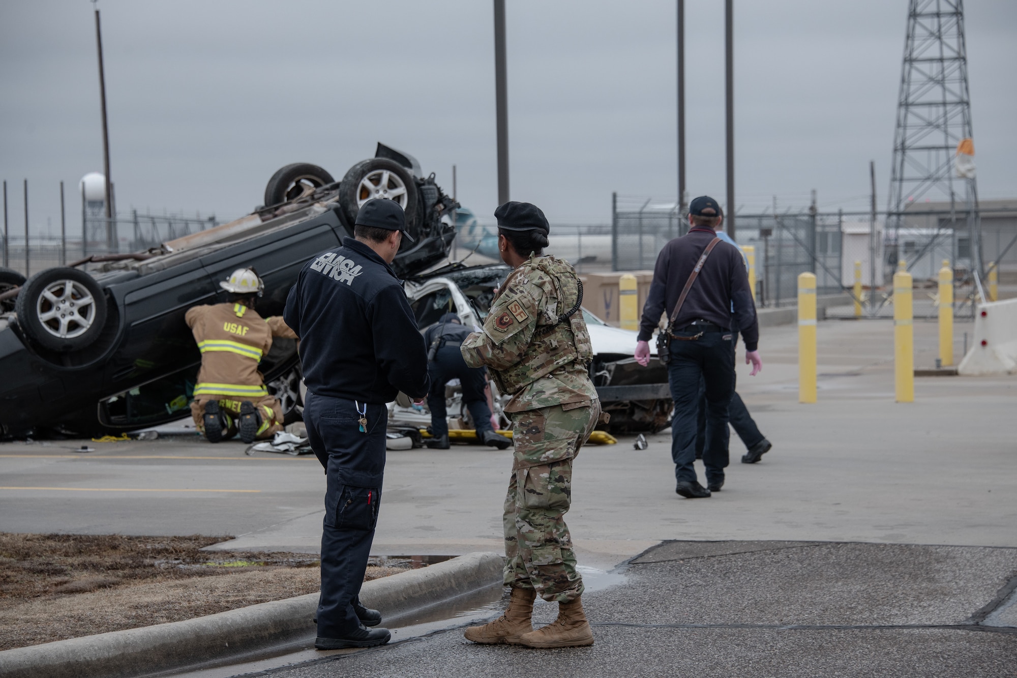 two people watch as firefighters examine crashed cars during training exercise