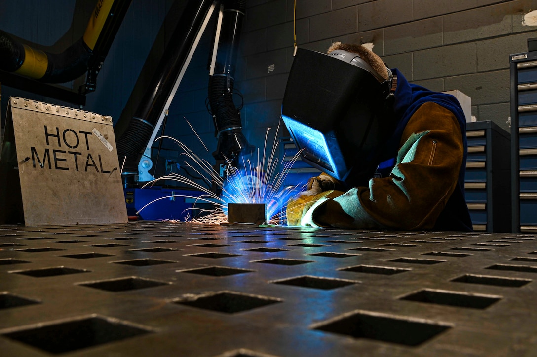 An airman wearing protective equipment welds metal as sparks fly.