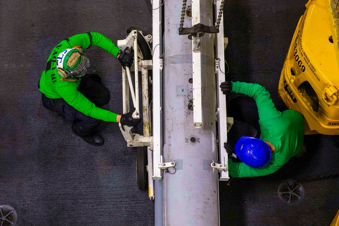 Two sailors secure a large piece of equipment.