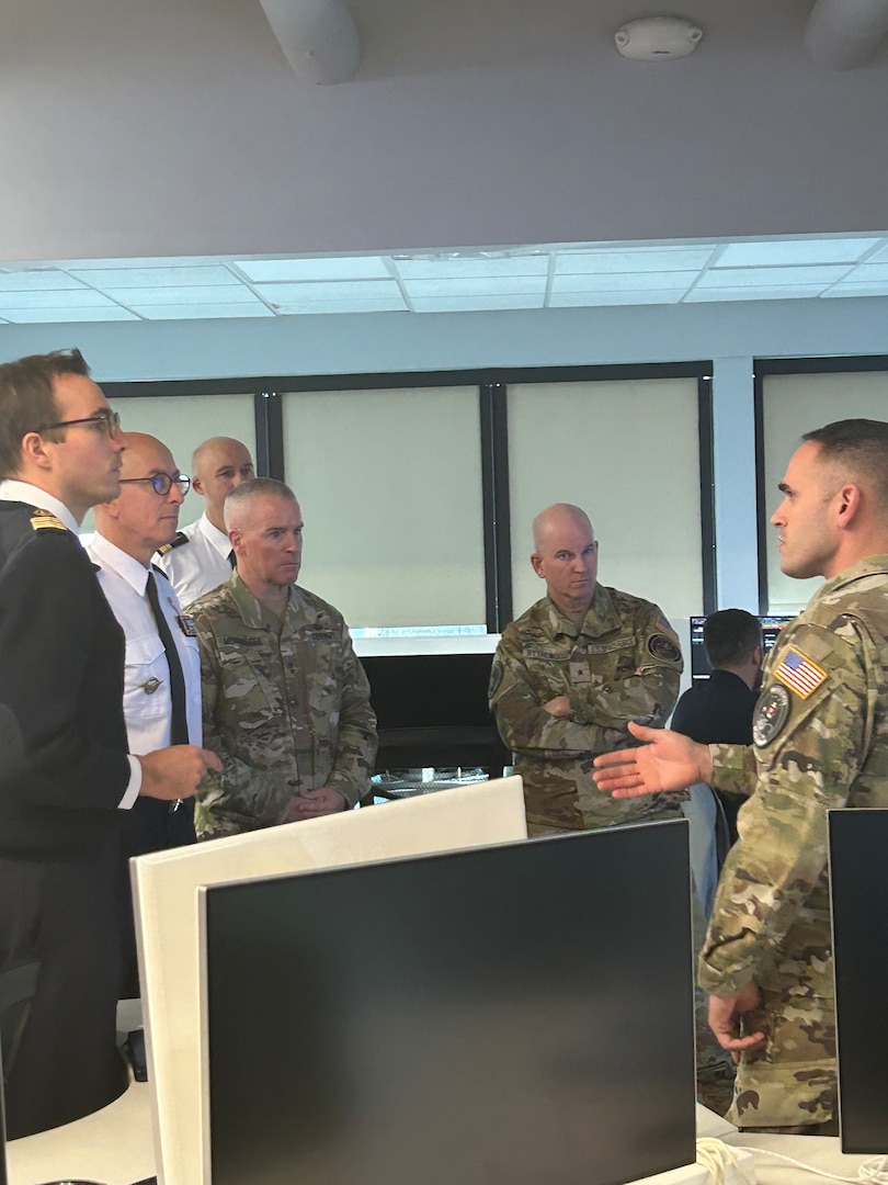 A group of five men listening to a man speaking