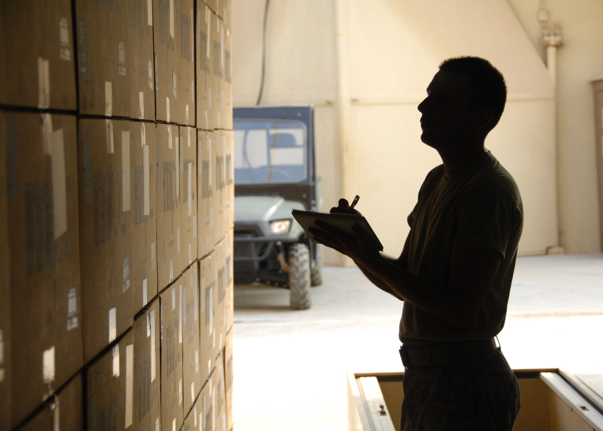 An airman holding a clipboard inspects some boxes.