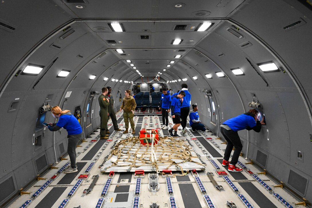 People walk around the interior of a large aircraft and look out windows.