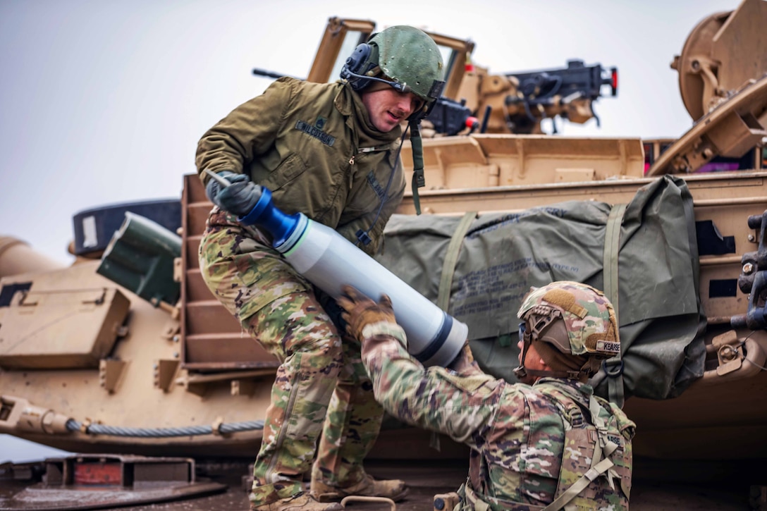 Two service members load ammunition onto a tank during an exercise.