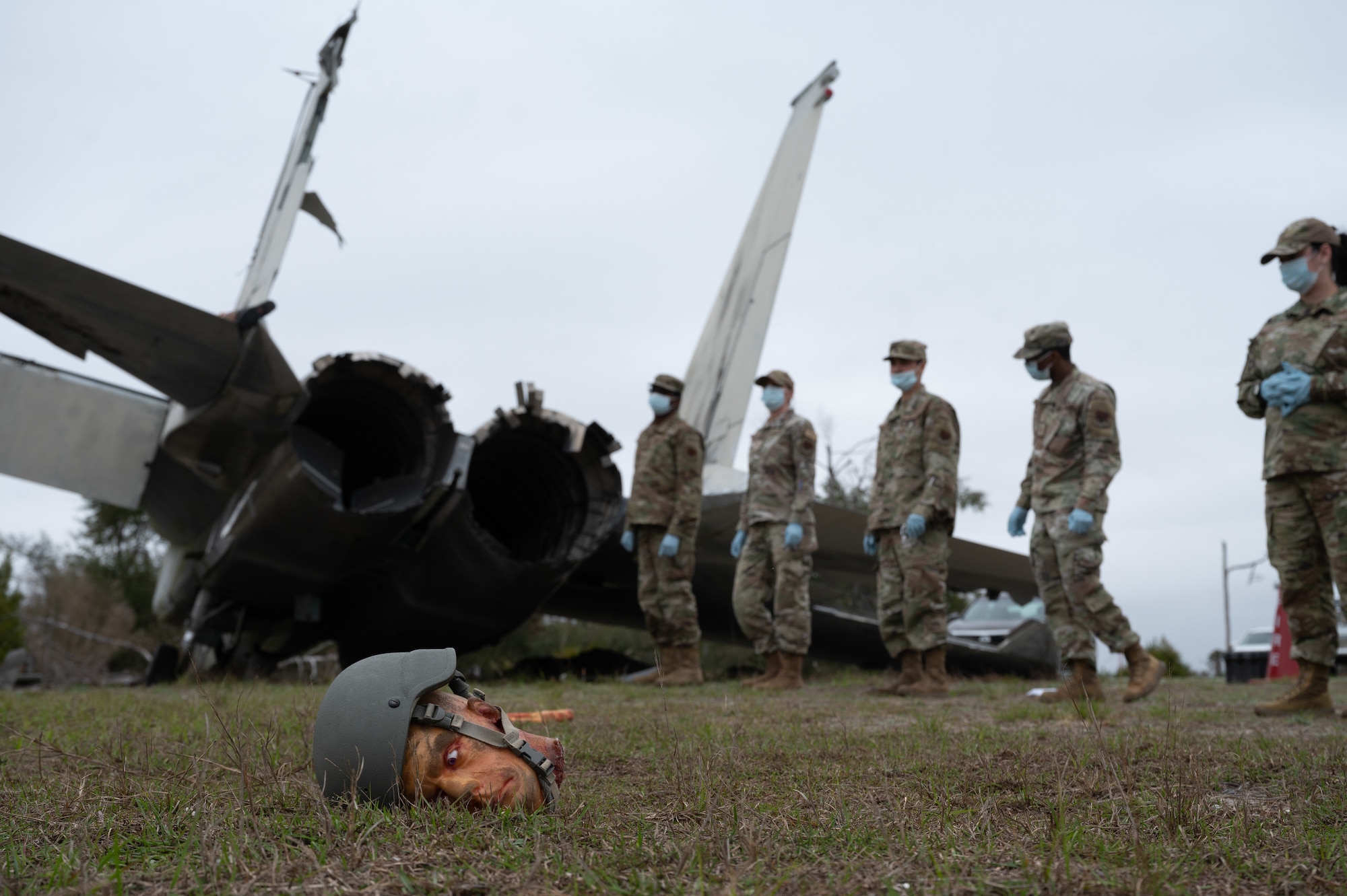 Airmen walk in a field next to a simulates plane crash