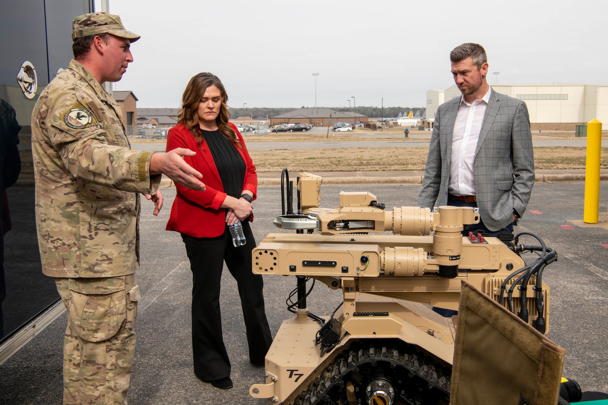 A military member briefs a man and a woman on an explosive ordnance disposal robot's capabilities.
