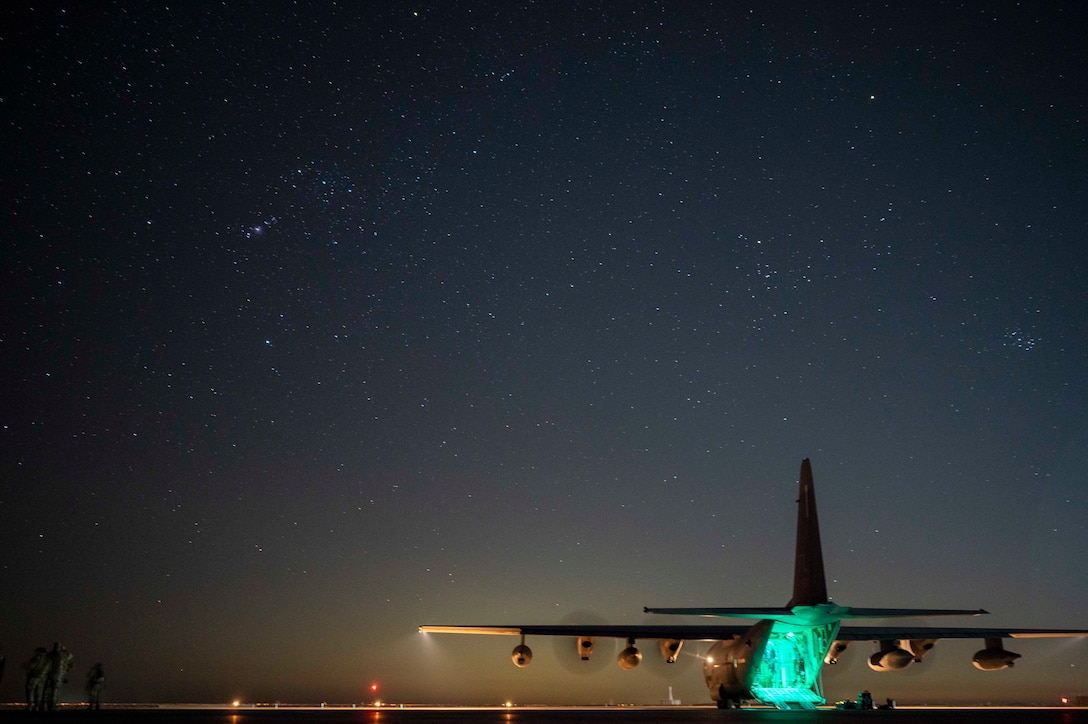 A military aircraft is parked on a runway, illuminated by the night sky and a green light.