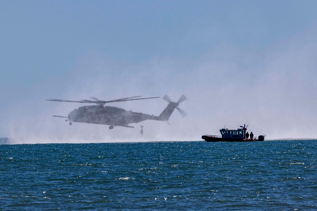 A Marine jumps out of a helicopter into water near a boat.