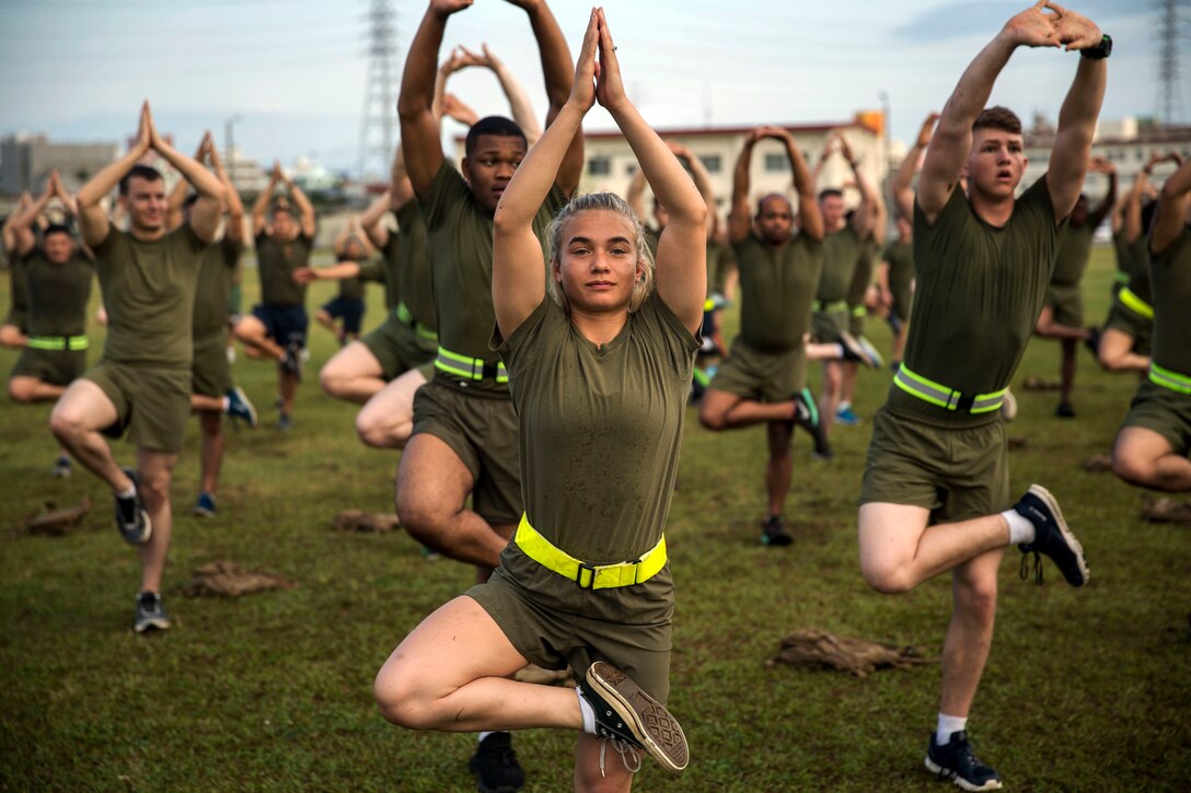 Service members assume yoga poses in a field.