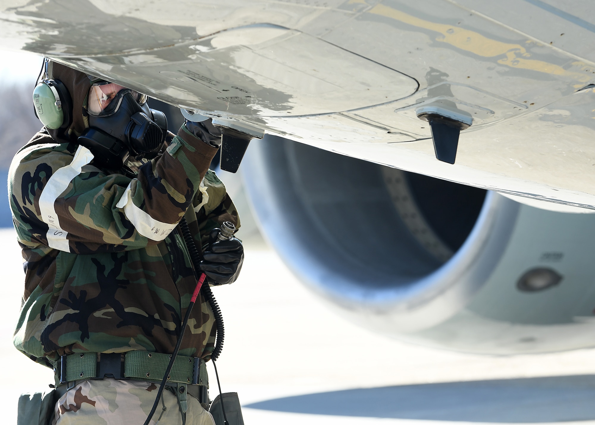 Airman in MOPP gear checks wing of aircraft