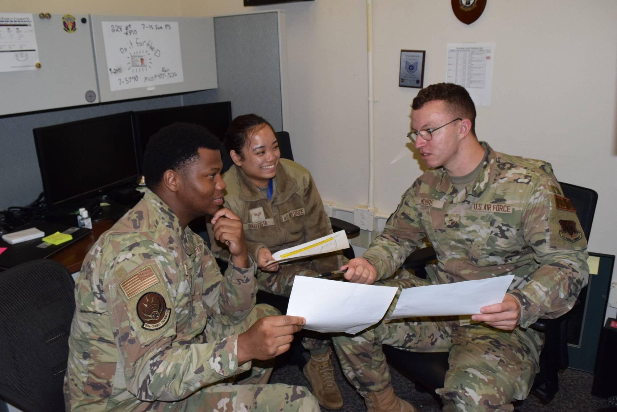 photo of three U.S. Air Force Airmen in uniform sitting in an office looking at paperwork