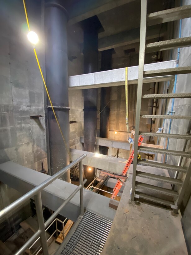 Inside a dimly lit concrete structure with a ladder to the right and a large metal pipe to the left.