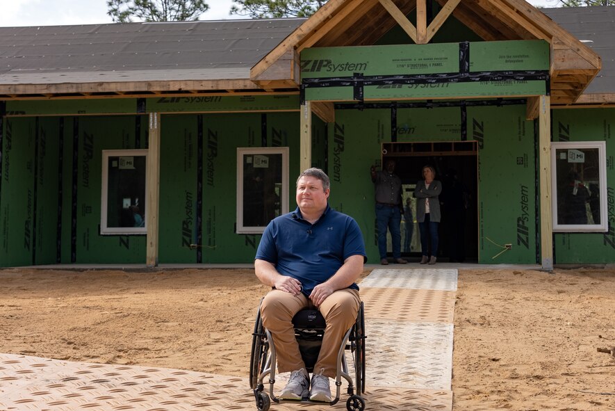 a man sits in a wheelchair in front of his house under construction