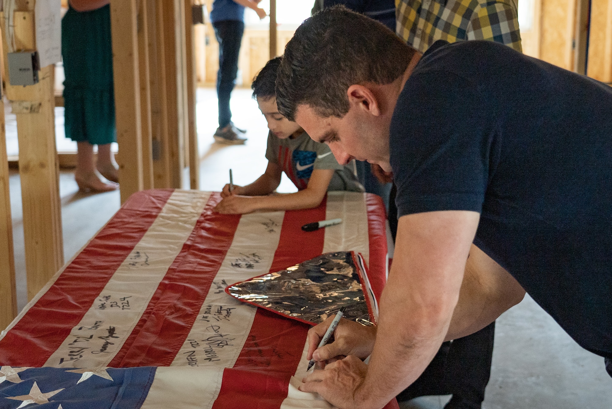 a man and a kid write their signature on an American flag