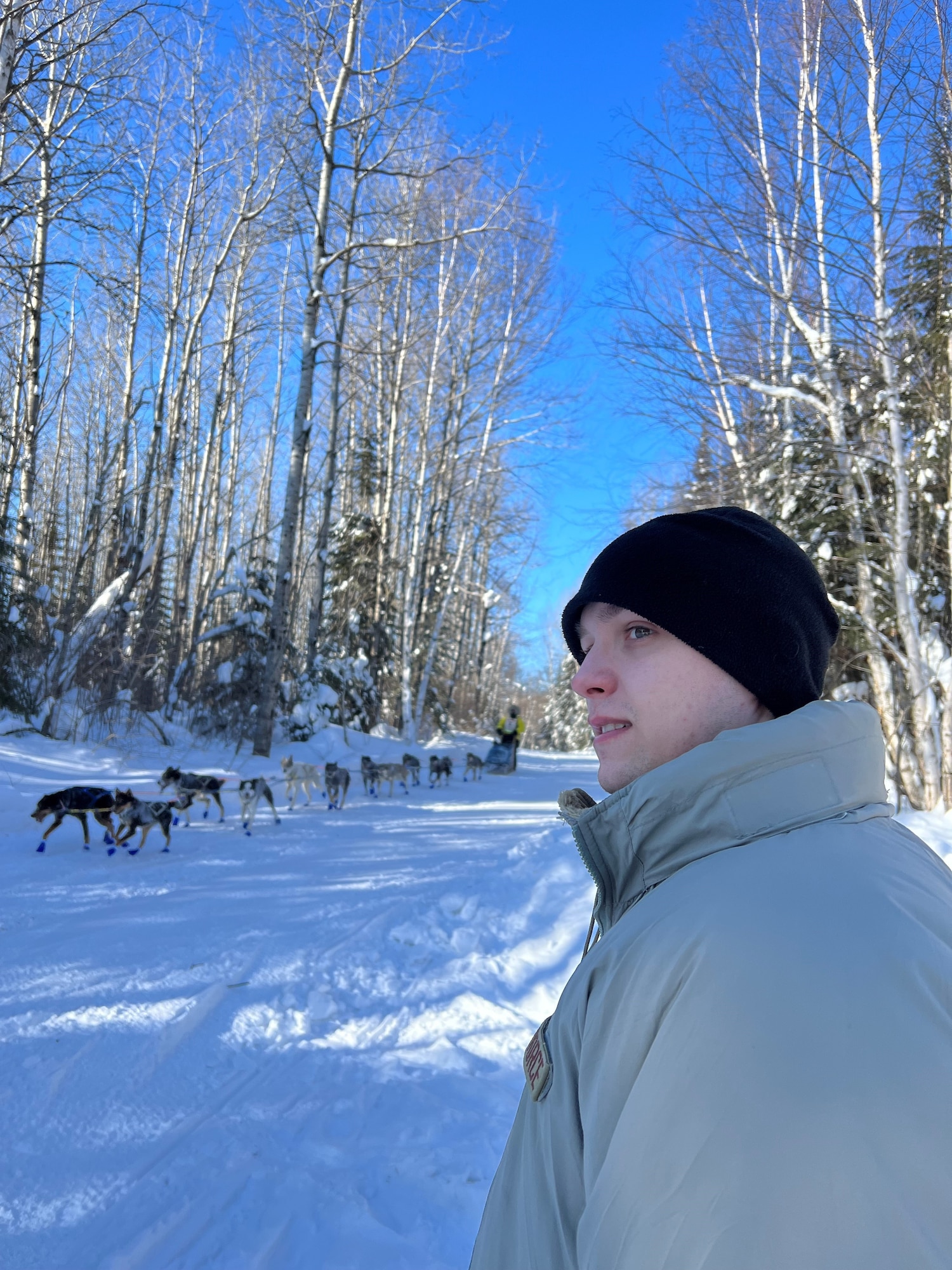 Radio Frequency Transmissions specialist, Airman 1st Class Nash Tahtinen, 148th Fighter Wing, Minnesota Air National Guard, observes a musher and sled dog team pass as part of a winter training exercise in Northern Minnesota on January 30, 2023. Communications experts from the Minnesota National Guard, 133rd Airlift Wing and 148th Fighter Wing established a camp, including tents and communications equipment, in subzero temperatures in conjunction with the 2023 John Beargrease Sled Dog Marathon. The winter exercise allowed soldiers and airmen to set up, operationalize and troubleshoot equipment in adverse conditions in a remote location.