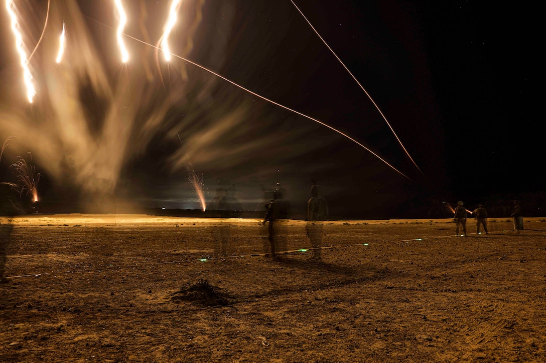 Marines fire flares into the sky at night.