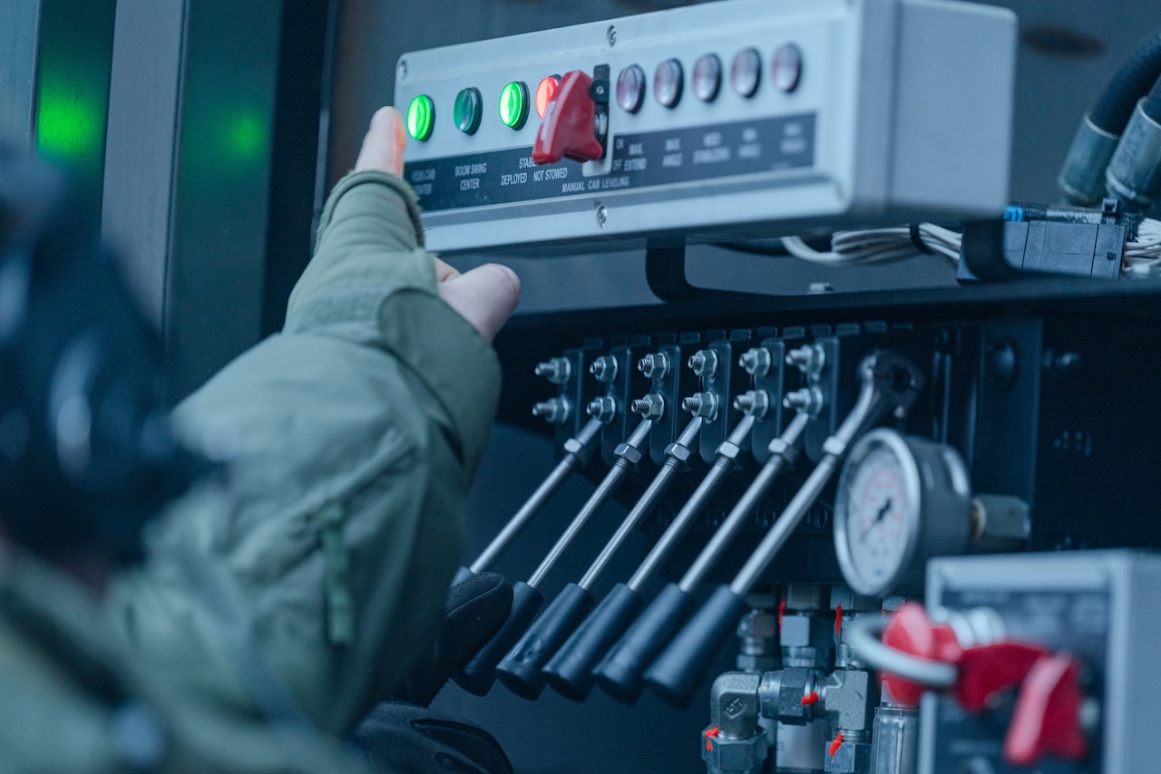 A person reaches to a green-lit button  on a control panel.