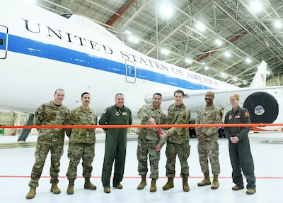 Men and women prepare to cut a ribbon while standing in front of an E-4B aircraft