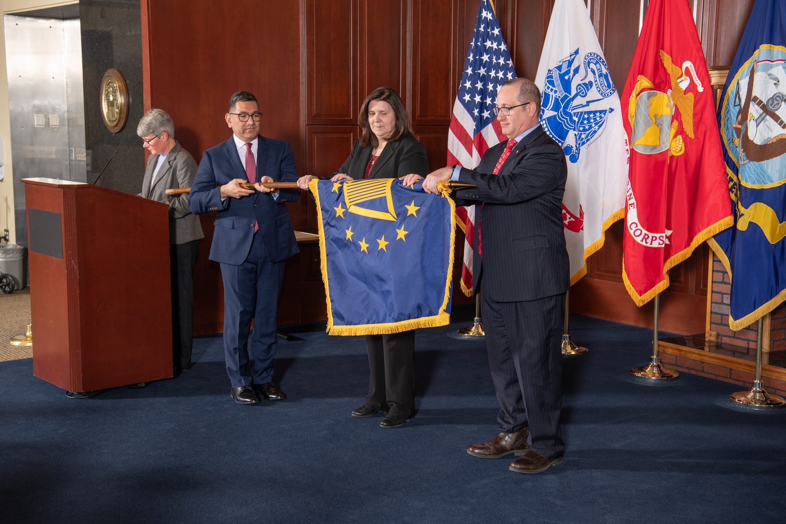 three individuals unfurl a senior executive service flag