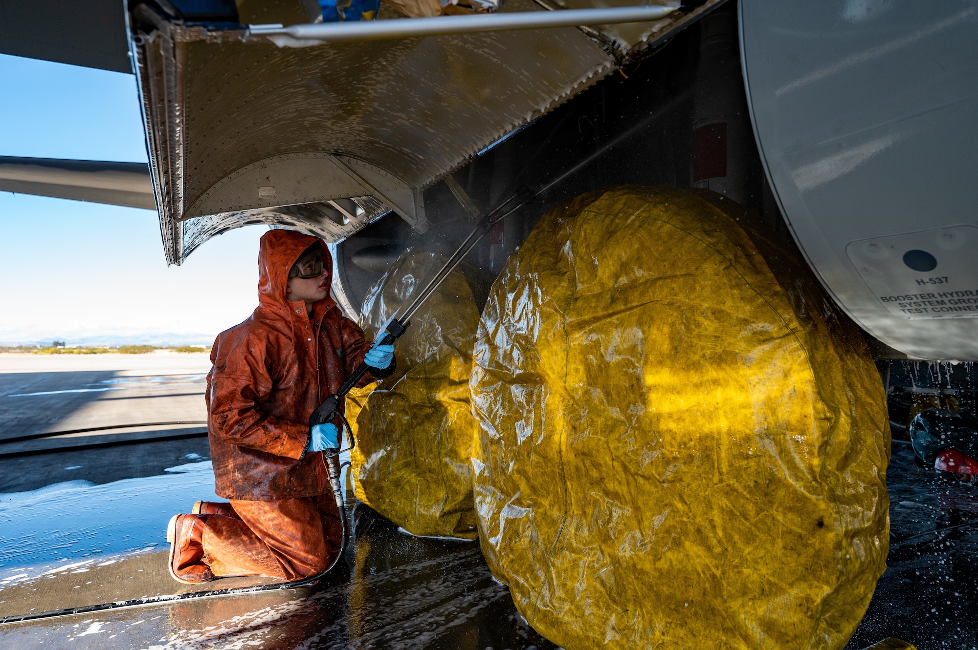 photo of a service member donning personal protective equipment washing underneath a large military aircraft