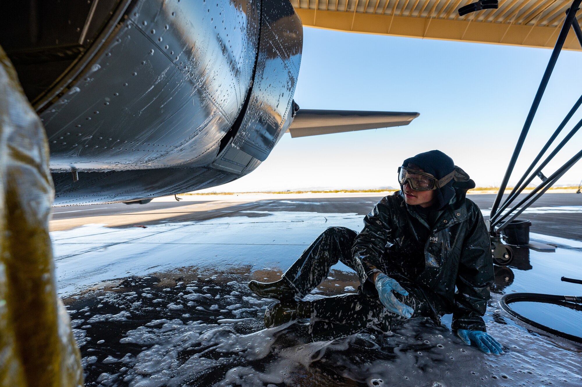 photo of a service member donning personal protective equipment washing underneath a large military aircraft