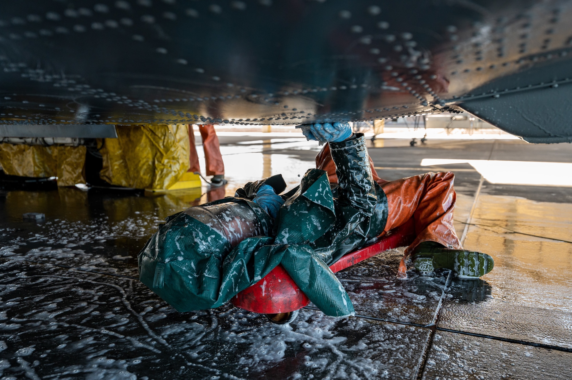 photo of a service member donning personal protective equipment washing underneath a large military aircraft