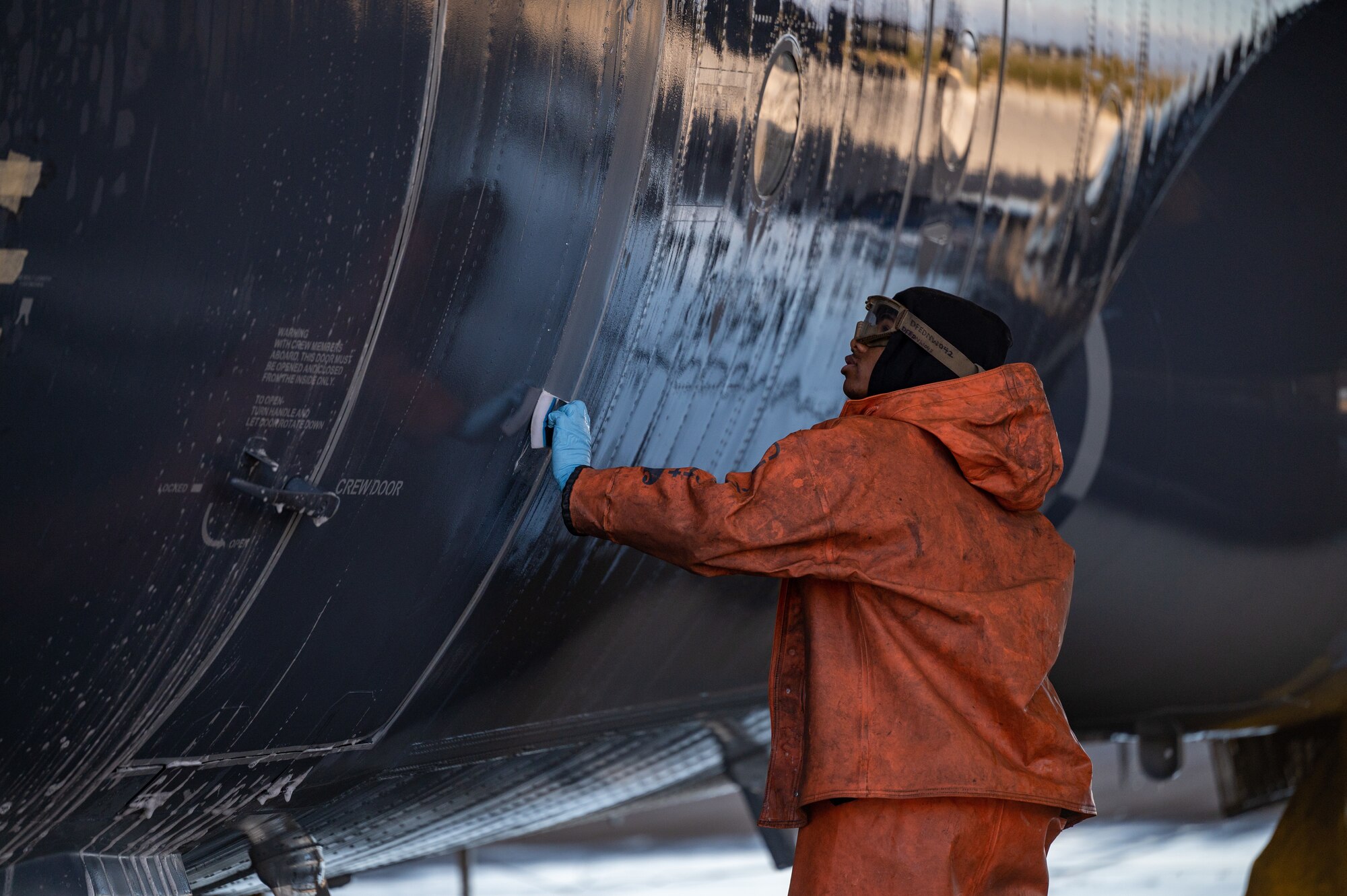 photo of a service member donning personal protective equipment and cleaning a large military aircraft