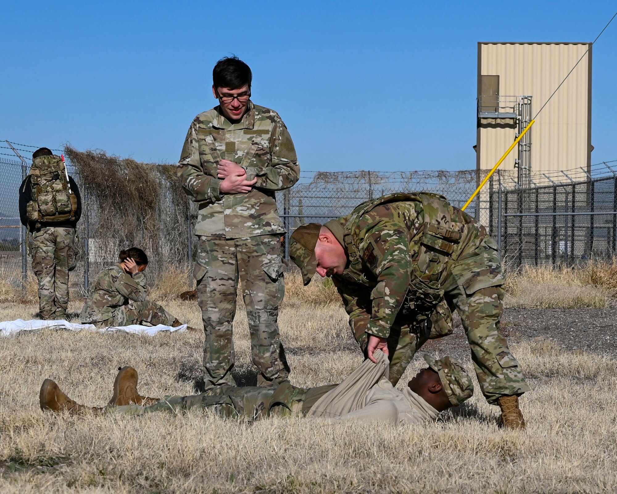 two Air Force Airmen provide medical care to a simulated victim outside in a dried grass area