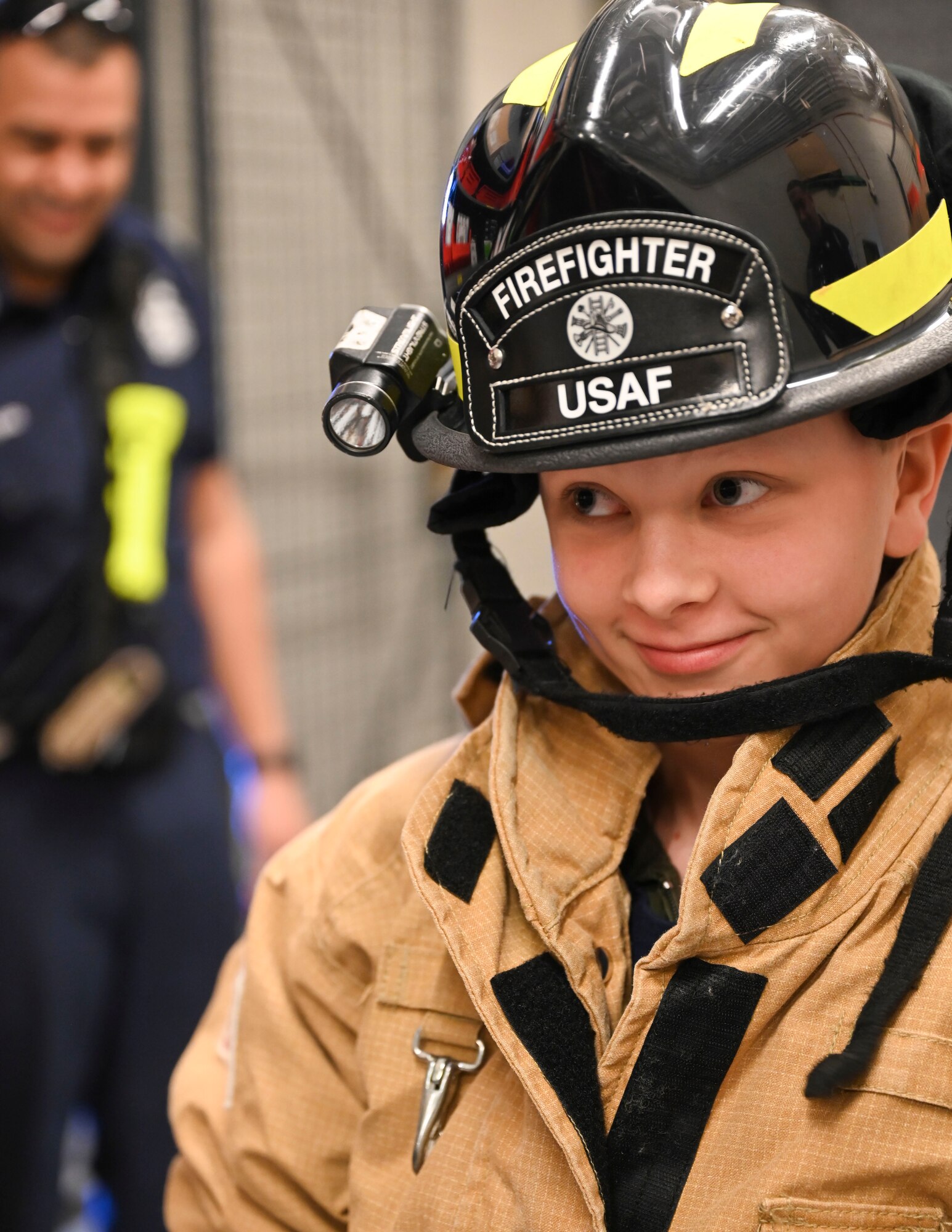 Boy looks out from underneath a firefighters helmet.