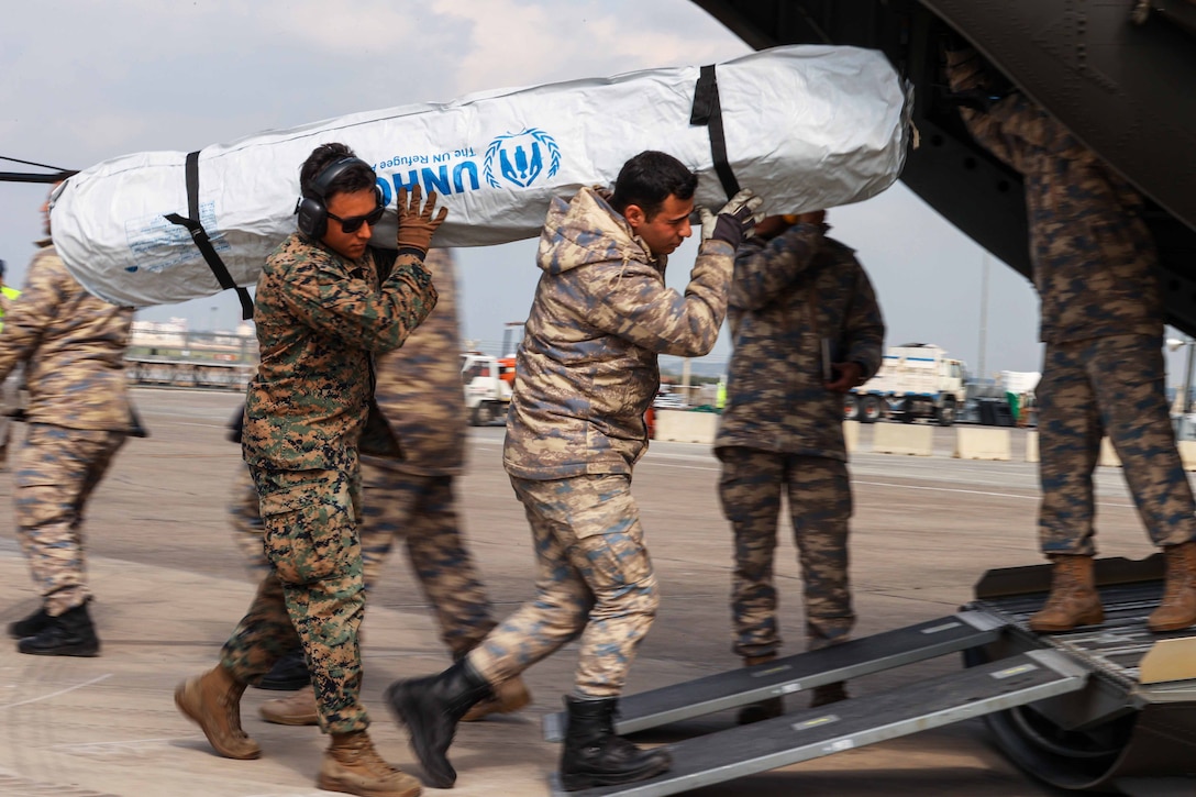 A Marine helps a Turkish soldier carry supplies onto a helicopter.