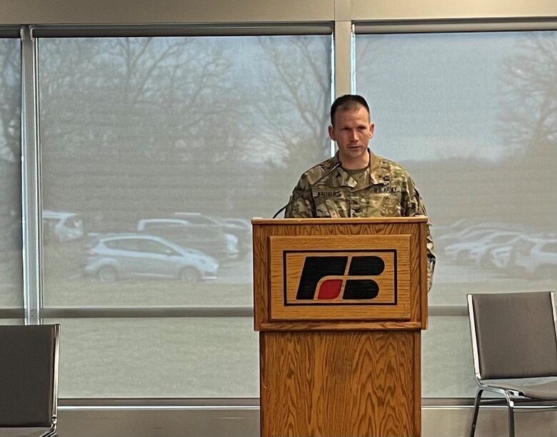 A man in a military uniform stands behind a podium and speaks to a crowd.