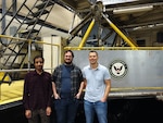 Mechanical engineers Jeeven Hugh (left), Roger Kleinmann (center) and team lead Alexander Tsarev (right), all with Naval Surface Warfare Center, Carderock Division’s Maritime Systems Hydromechanics Branch, pose in front of Carriage 2 at the east end of the David Taylor Model Basin in West Bethesda, Md., on Feb. 15, 2023. (Photo provided by Roger Kleinmann, Alexander Tsarev and Jeeven Hugh)