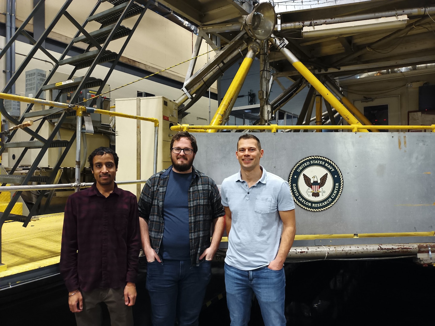 Mechanical engineers Jeeven Hugh (left), Roger Kleinmann (center) and team lead Alexander Tsarev (right), all with Naval Surface Warfare Center, Carderock Division’s Maritime Systems Hydromechanics Branch (Code 881), pose in front of Carriage 2 at the east end of the David Taylor Model Basin in West Bethesda, Md., on Feb. 15, 2023. (Photo provided by Roger Kleinmann, Alexander Tsarev and Jeeven Hugh)