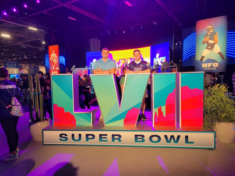 Two men poses on top of a giant sign that reads “Super Bowl LVII.”