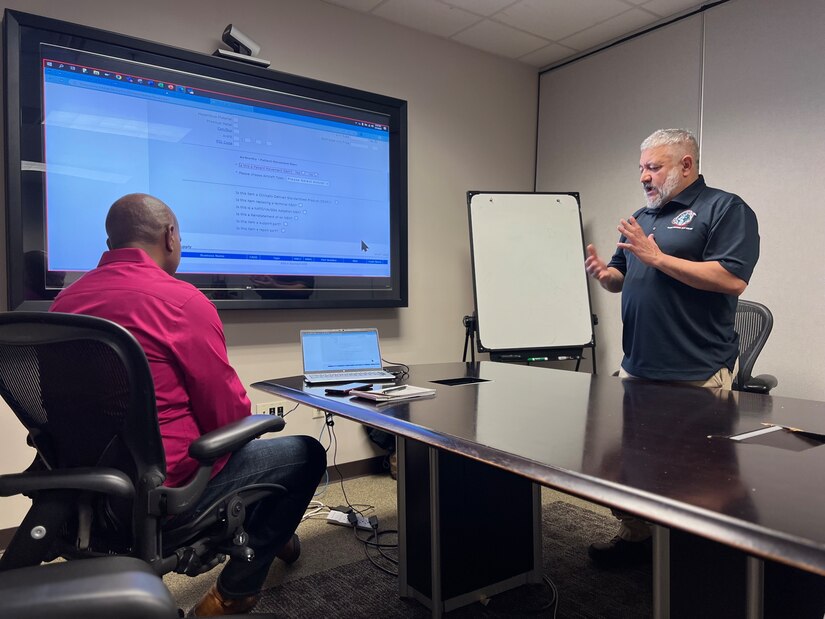 Juan Flores, right, a general supply specialist with the U.S. Army Medical Materiel Agency’s Business Support Office, leads a discussion during online training on the Defense Medical Logistics Item Identification System, or DMLIIS. Also pictured is Matthew Diggs, a supply management specialist for the BSO. Flores and Diggs have been collaborating with Defense Health Agency’s Medical Logistics Directorate to provide DMLIIS training on an ongoing basis for supply specialists and clinical analysts.