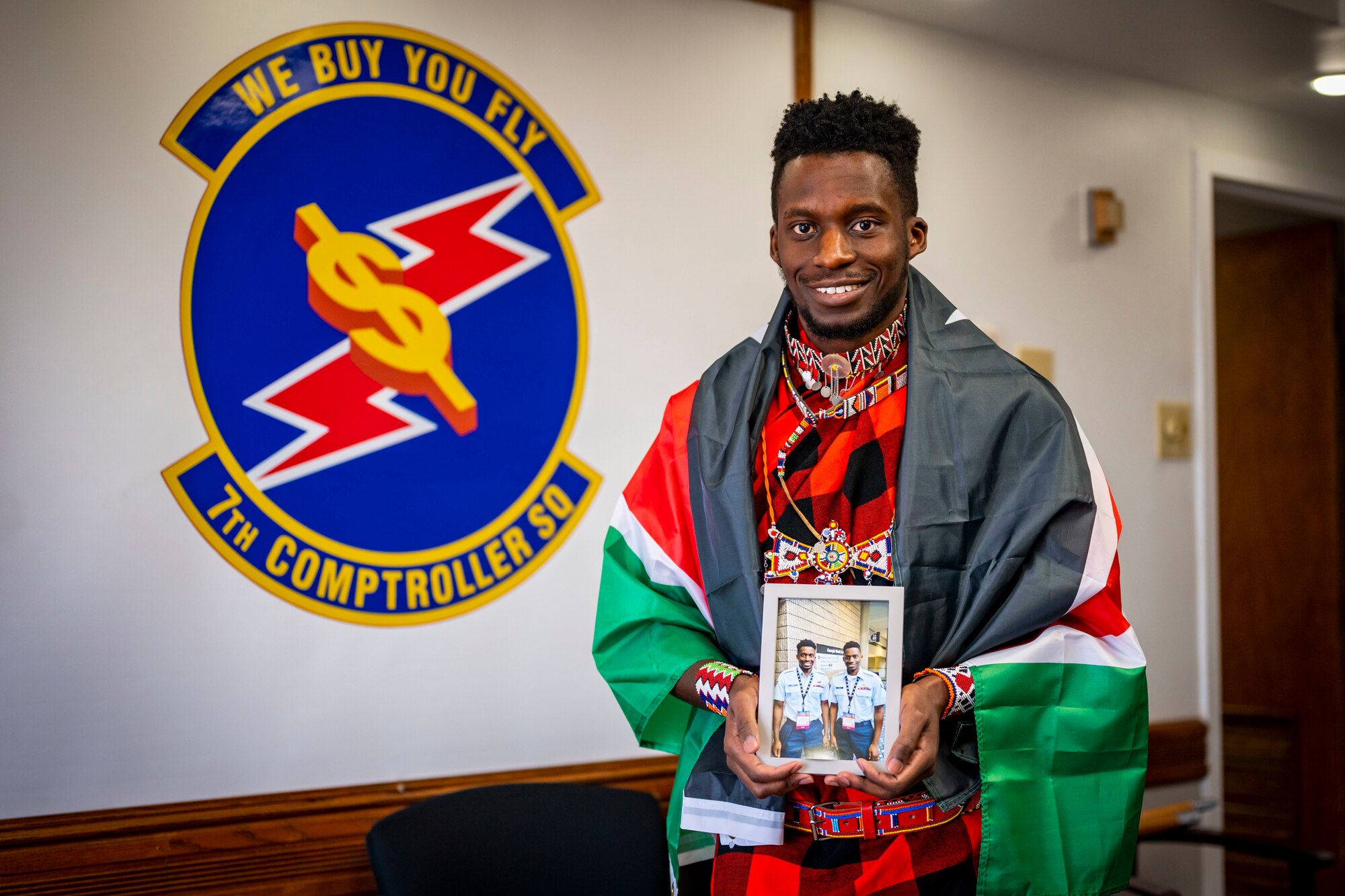 U.S. Air Force Senior Airman Daniel Omwoha, 7th Comptroller Squadron financial analyst technician, holds a photo of him and his brother while wearing a traditional Kenyan dress during Black History Month at Dyess Air Force Base, Texas, Feb. 9, 2023. Omwoha was born and raised in Nakuru, Kenya, in a family of 6. His journey is unique, joining the Air Force alongside his identical twin brother, who is currently stationed at Langley AFB, also in the finance career field. Omwoha takes pride in his job and believes in getting better every day and helping anybody in need. (U.S. Air Force photo by Senior Airman Leon Redfern)