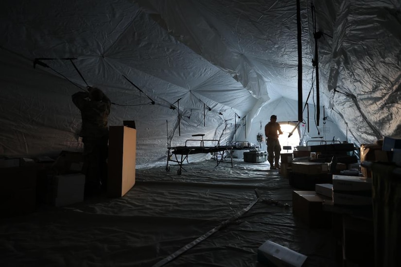 The silhouette of a man standing inside of a tent is shown.