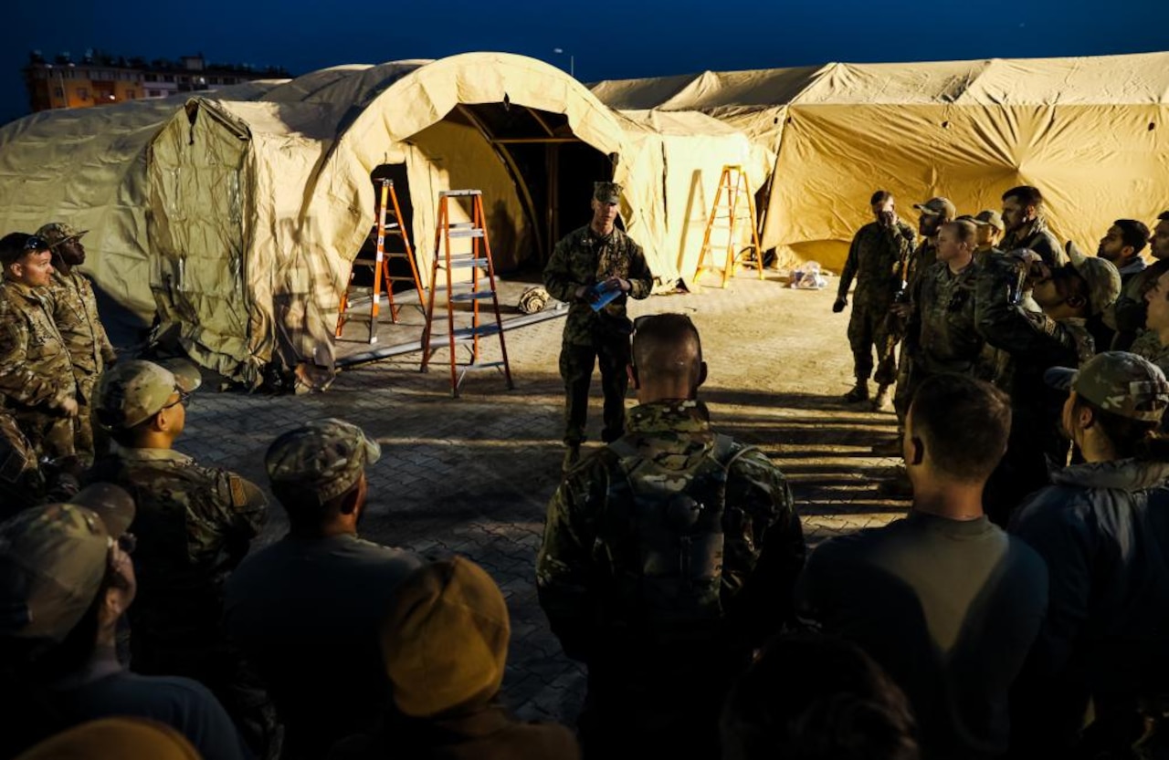 Men and women in military uniform stand in front of tents.