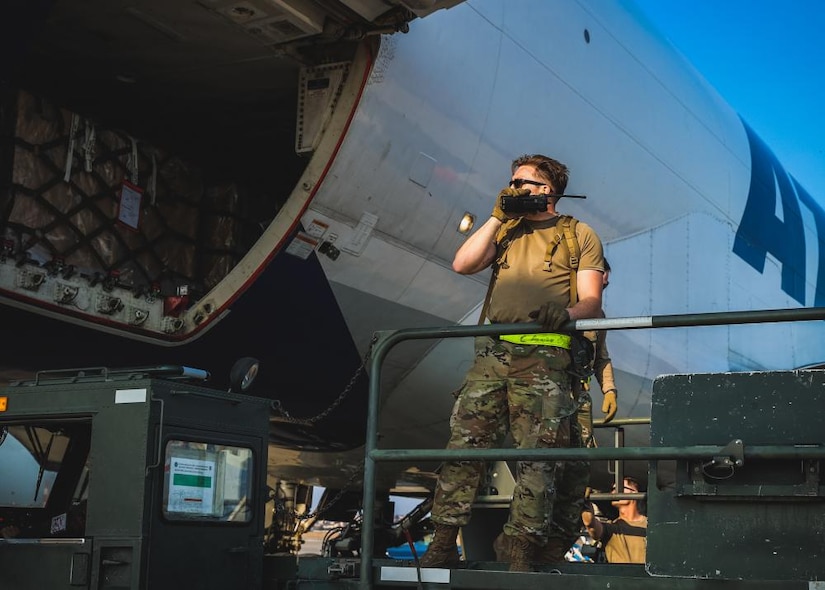 A man in military uniform, directs a cargo truck.