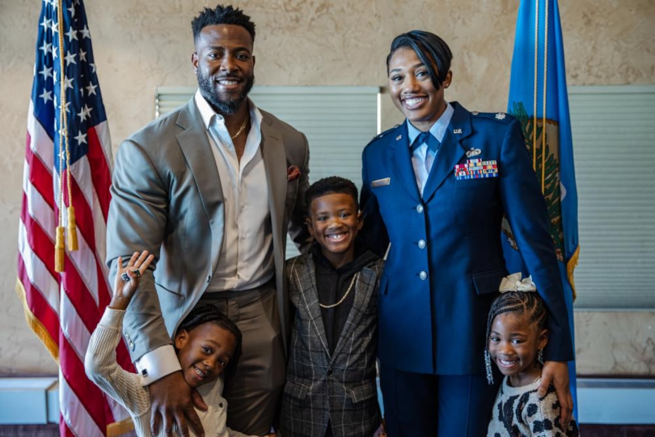 A female uniformed service member smiles while standing with her family.