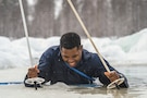 A soldier digs ski poles into ice to climb out of a body of water.