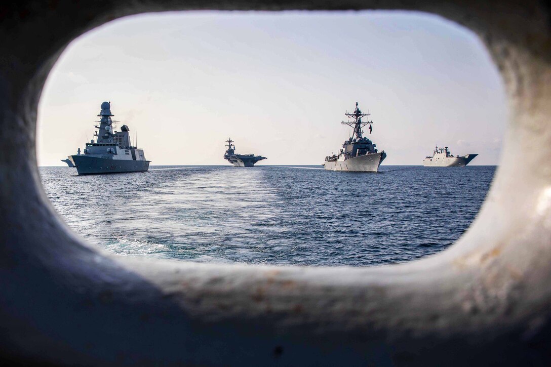 Several ships sail in formation are seen through a hole.