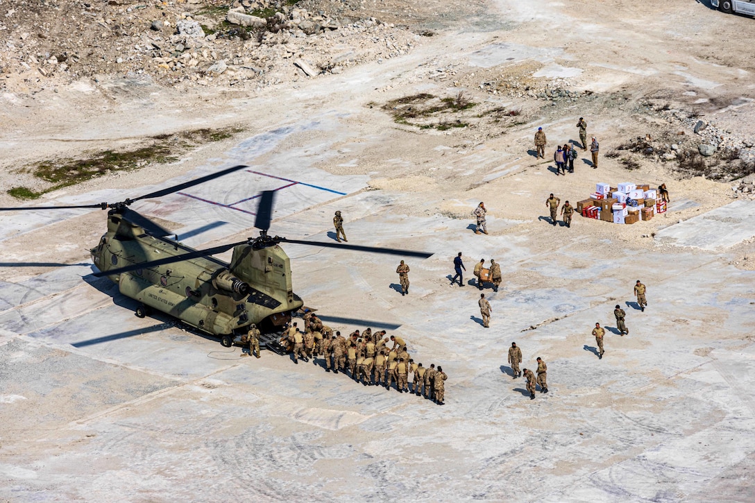 An aerial view of soldiers unloading relief supplies from a large helicopter.