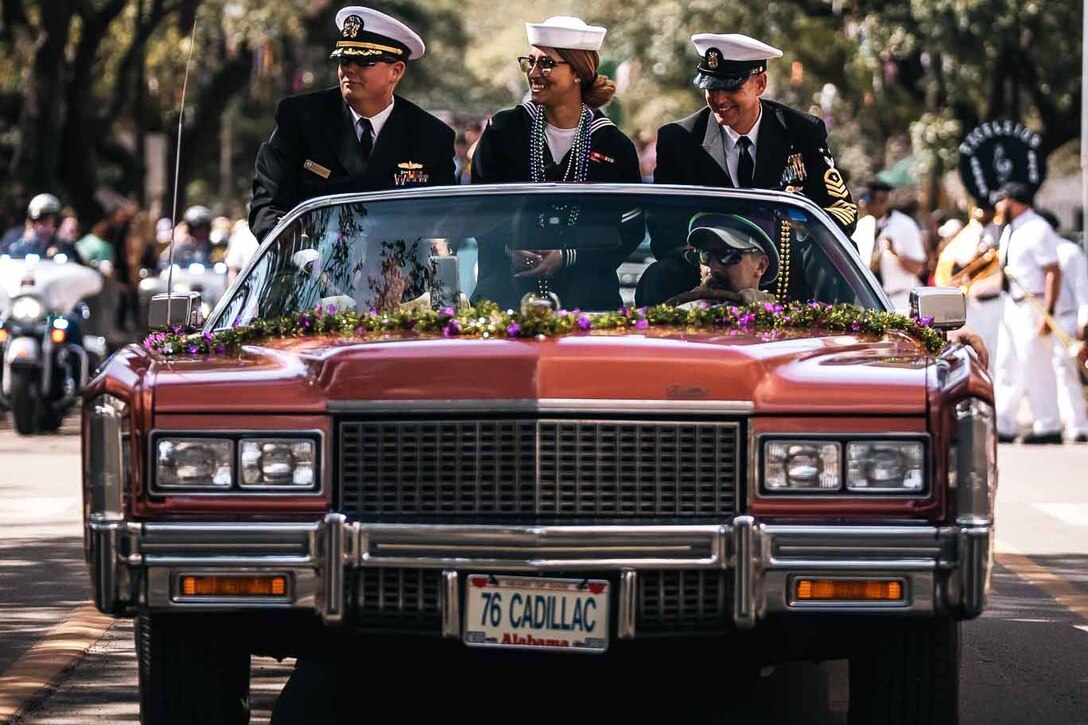 Three sailors smile as they sit in a Cadillac during a parade.