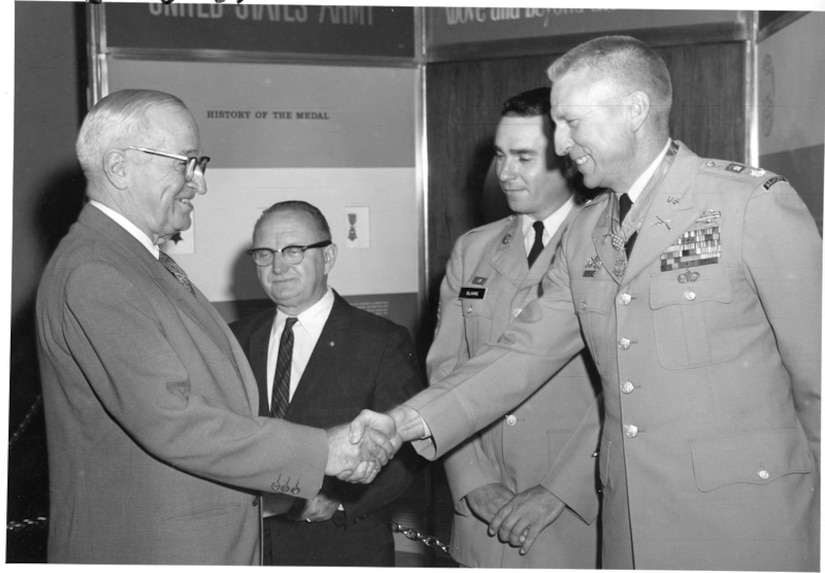 Two men shake hands while two other men stand near them