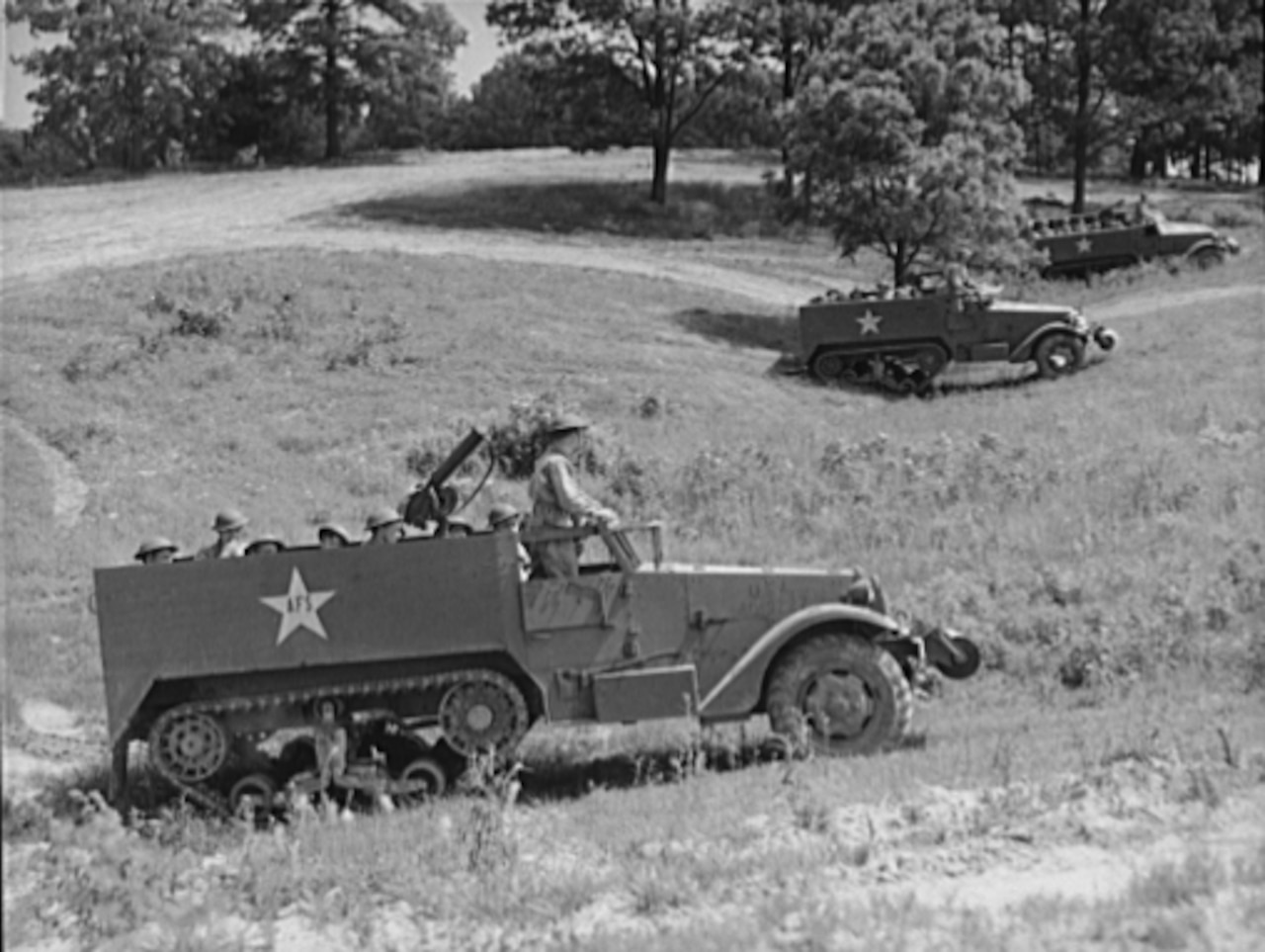 Three vehicles with both wheels and tank tread move through a field.